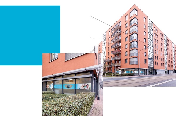 Modernes Wohn- und Geschäftsgebäude mit oranger Fassade und Straßenbahngleisen.