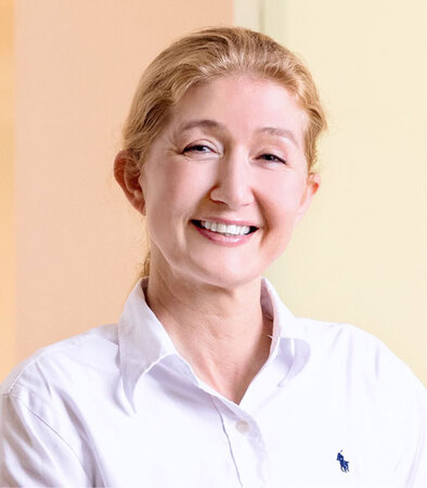 Porträt einer lächelnden Frau im weißen Hemd, freundliche Ausstrahlung, helle Umgebung.