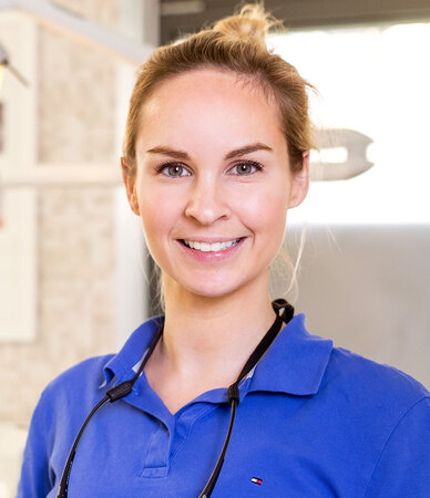 Junge Zahnärztin mit blauem Kittel und Stethoskop lächelt in moderner Zahnarztpraxis.