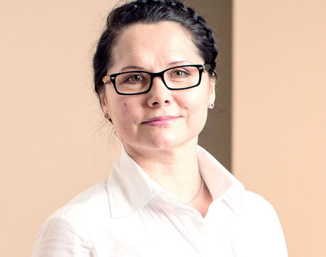 Porträt einer Frau mit Brille und weißer Bluse, neutraler Hintergrund, Business-Look.